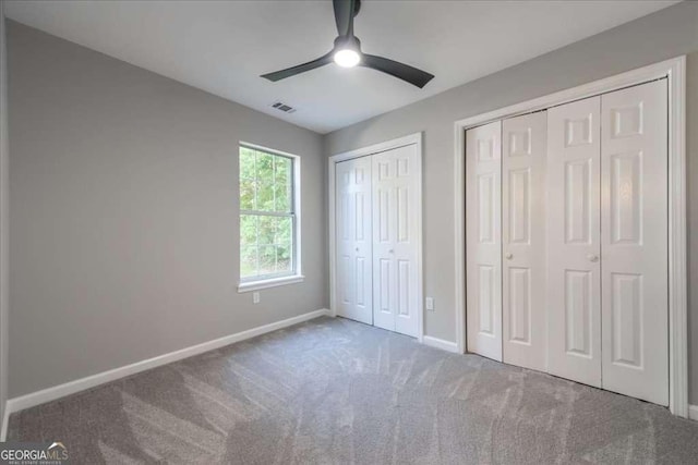 unfurnished bedroom with carpet, ceiling fan, and multiple closets