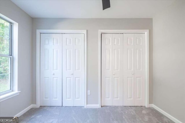 unfurnished bedroom with carpet flooring, two closets, and ceiling fan