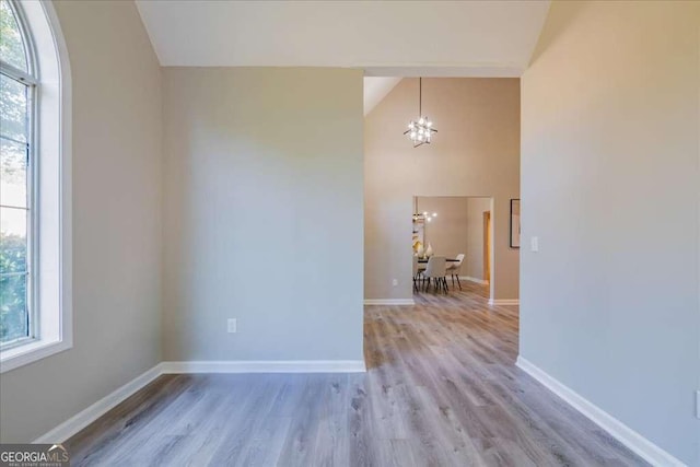 spare room with light hardwood / wood-style floors, vaulted ceiling, and a notable chandelier