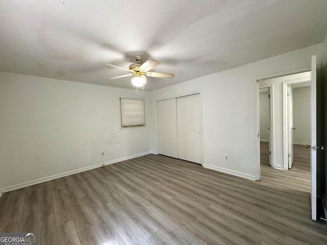 unfurnished bedroom featuring ceiling fan, a closet, wood-type flooring, and a textured ceiling