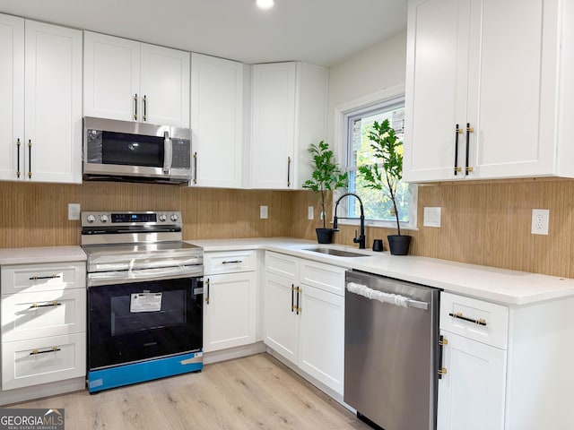 kitchen with sink, tasteful backsplash, appliances with stainless steel finishes, white cabinets, and light wood-type flooring