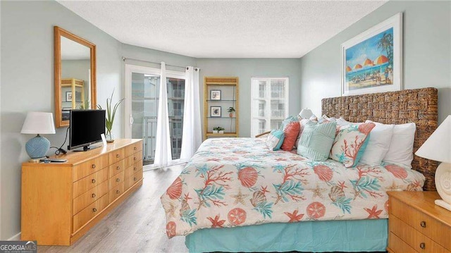 bedroom with access to exterior, light hardwood / wood-style floors, and a textured ceiling