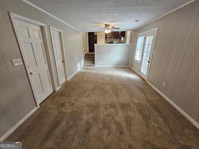 unfurnished room with carpet, a textured ceiling, ceiling fan, and wood walls