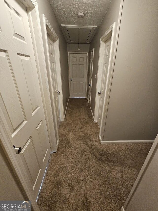 hallway with a textured ceiling and dark colored carpet