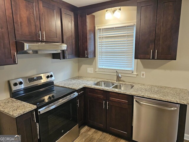 kitchen with sink, stainless steel appliances, light stone counters, dark brown cabinets, and light wood-type flooring