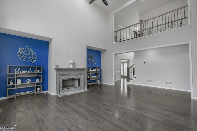 living room featuring a fireplace, built in shelves, dark wood-type flooring, and a high ceiling