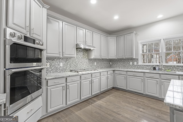 kitchen with sink, stainless steel appliances, light stone counters, light hardwood / wood-style flooring, and decorative backsplash