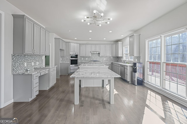 kitchen featuring light stone countertops, appliances with stainless steel finishes, dark hardwood / wood-style flooring, a notable chandelier, and gray cabinets