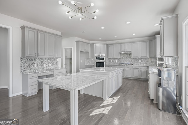 kitchen featuring gray cabinetry, a center island, dark hardwood / wood-style floors, light stone countertops, and appliances with stainless steel finishes