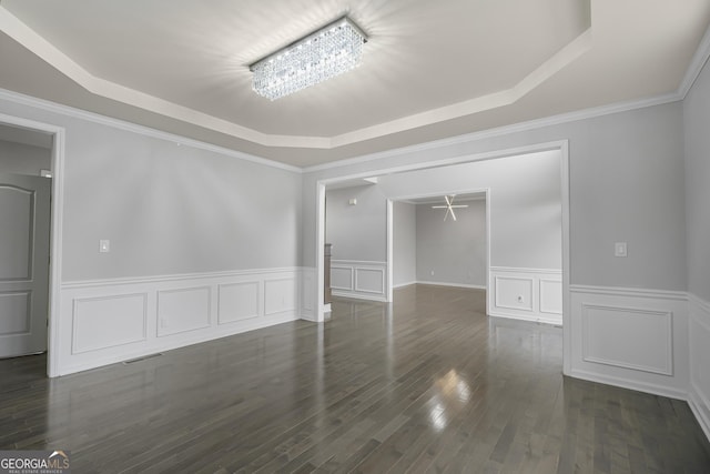 spare room with a tray ceiling, crown molding, dark wood-type flooring, and a notable chandelier