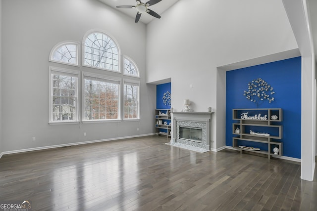 living room featuring a premium fireplace, dark hardwood / wood-style flooring, ceiling fan, and a high ceiling