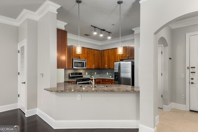 kitchen featuring pendant lighting, backsplash, dark stone counters, appliances with stainless steel finishes, and kitchen peninsula