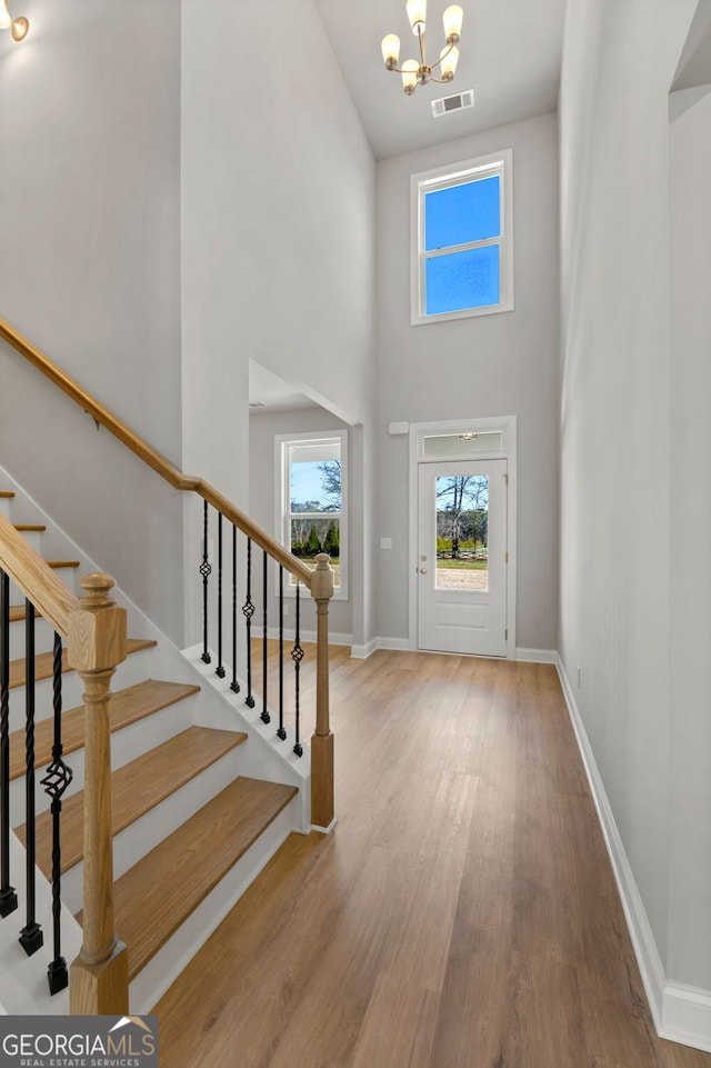 entryway with light wood-type flooring, a towering ceiling, and a chandelier