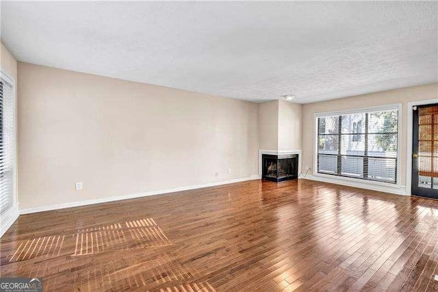 unfurnished living room featuring hardwood / wood-style floors, a multi sided fireplace, and a textured ceiling