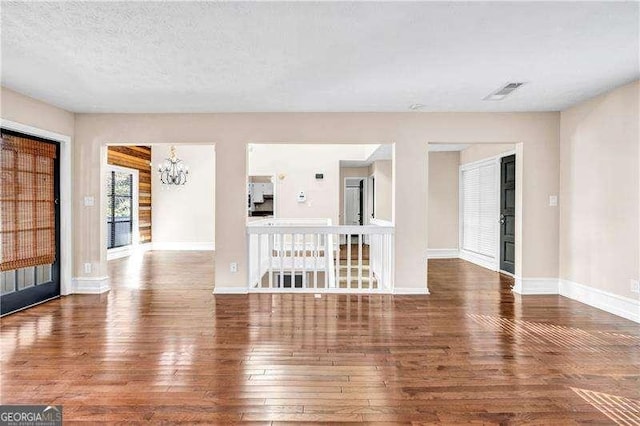 unfurnished living room with dark wood-type flooring, a textured ceiling, and a notable chandelier