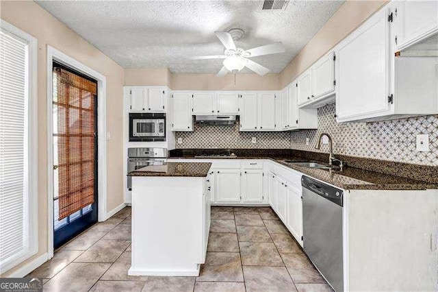 kitchen featuring appliances with stainless steel finishes, a kitchen island, sink, dark stone countertops, and white cabinetry