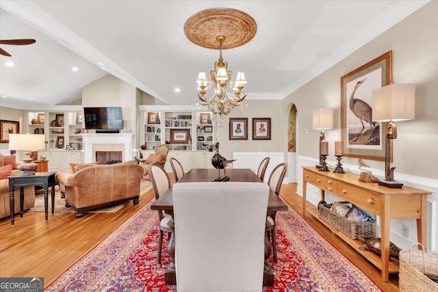 dining area with ceiling fan with notable chandelier, crown molding, vaulted ceiling with beams, built in features, and wood-type flooring