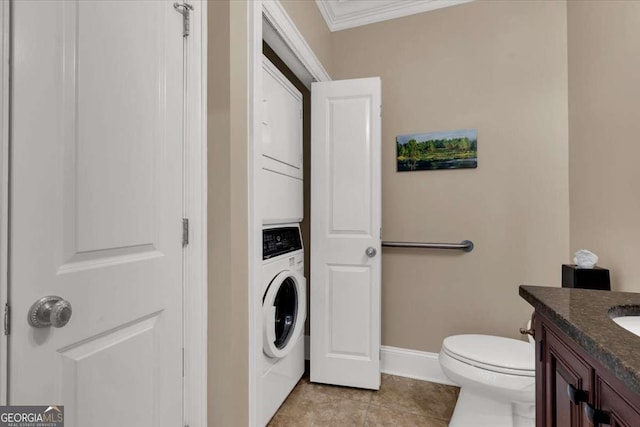 bathroom featuring vanity, crown molding, stacked washer / dryer, tile patterned flooring, and toilet