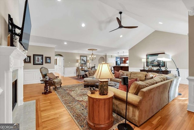 living room with light wood-type flooring, ceiling fan with notable chandelier, crown molding, and lofted ceiling