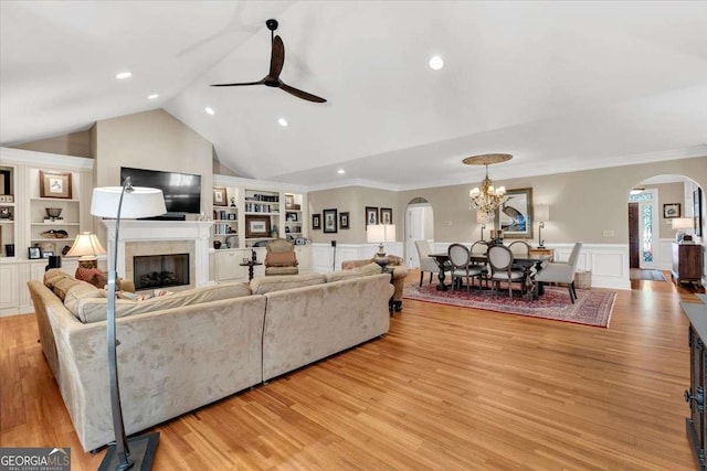 living room with ceiling fan with notable chandelier, vaulted ceiling, light hardwood / wood-style flooring, built in shelves, and ornamental molding