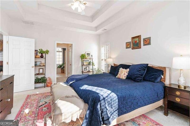 bedroom with a raised ceiling, ceiling fan, and light carpet