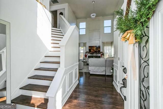 foyer entrance featuring a fireplace, a towering ceiling, and dark wood-type flooring