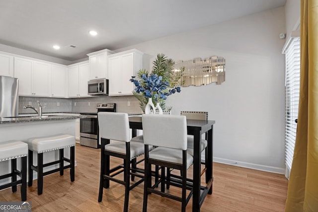 kitchen with appliances with stainless steel finishes, tasteful backsplash, light stone counters, light hardwood / wood-style floors, and white cabinetry