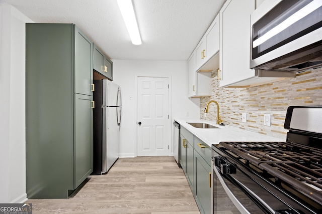 kitchen featuring backsplash, sink, light hardwood / wood-style floors, white cabinetry, and stainless steel appliances