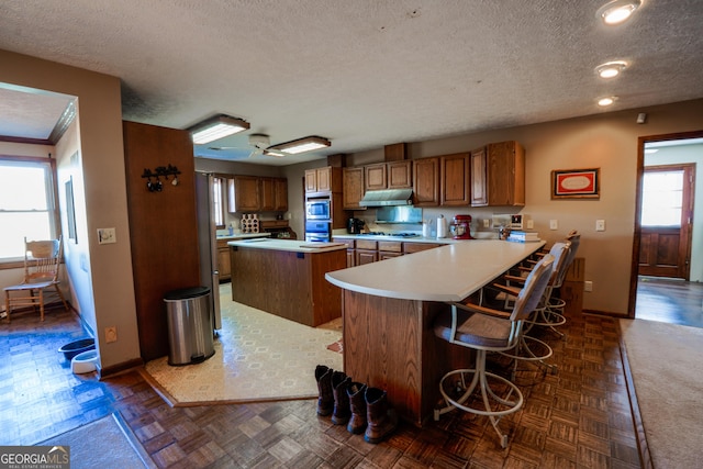 kitchen featuring dark parquet floors, a kitchen island, a kitchen bar, and kitchen peninsula