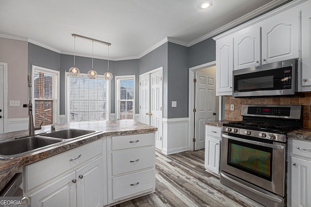 kitchen featuring stainless steel appliances, white cabinets, wainscoting, crown molding, and light wood-type flooring