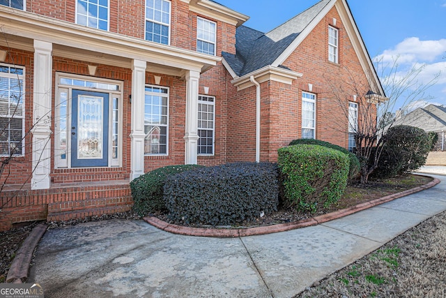 entrance to property featuring brick siding and roof with shingles