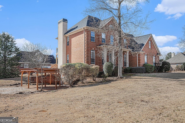 view of side of property with a lawn, brick siding, and a chimney