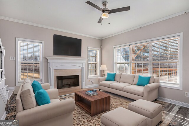 living room featuring crown molding, baseboards, a premium fireplace, wood finished floors, and a ceiling fan