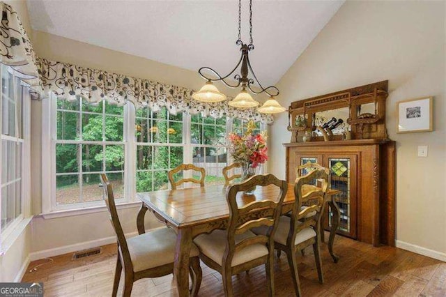 dining area featuring hardwood / wood-style flooring, vaulted ceiling, and a notable chandelier