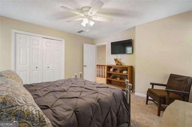 bedroom featuring ceiling fan, a closet, light colored carpet, and a textured ceiling