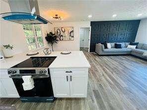 kitchen featuring electric stove, white cabinetry, light hardwood / wood-style floors, and wall chimney range hood