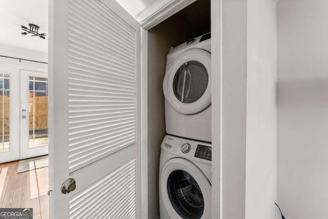 laundry area featuring wood-type flooring, french doors, and stacked washing maching and dryer