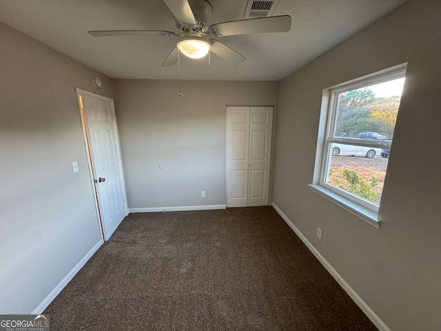 unfurnished bedroom with ceiling fan and dark colored carpet