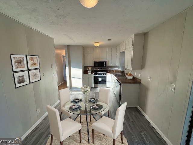 dining area with dark hardwood / wood-style floors, sink, wood walls, and a textured ceiling