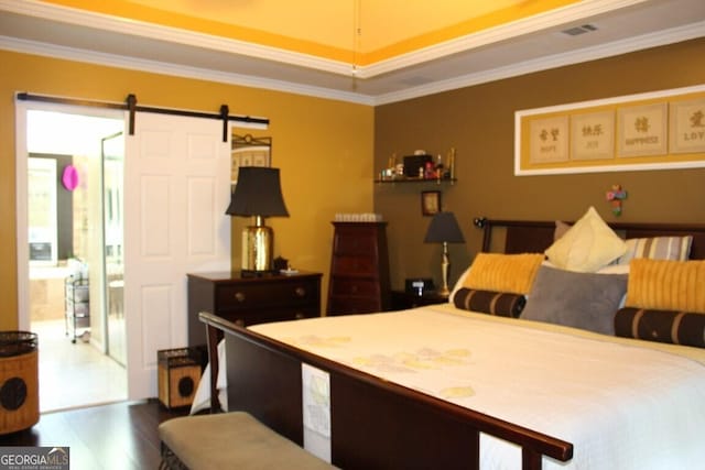 bedroom featuring wood-type flooring, a barn door, a tray ceiling, and ornamental molding