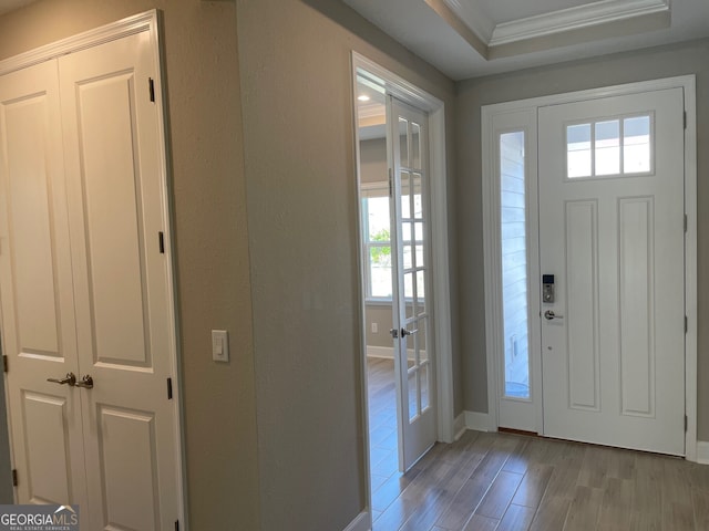 foyer entrance featuring baseboards, a raised ceiling, a textured wall, light wood-style flooring, and ornamental molding