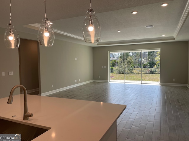 kitchen with baseboards, open floor plan, wood finished floors, a tray ceiling, and a sink