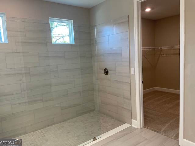 full bath featuring a walk in shower, a walk in closet, and baseboards