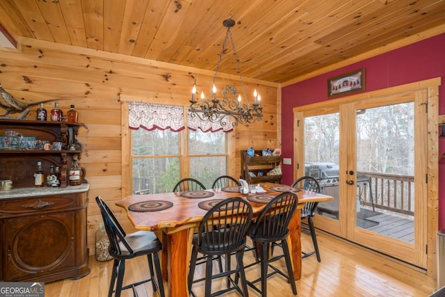 dining room featuring light hardwood / wood-style floors, wood ceiling, wooden walls, and a chandelier