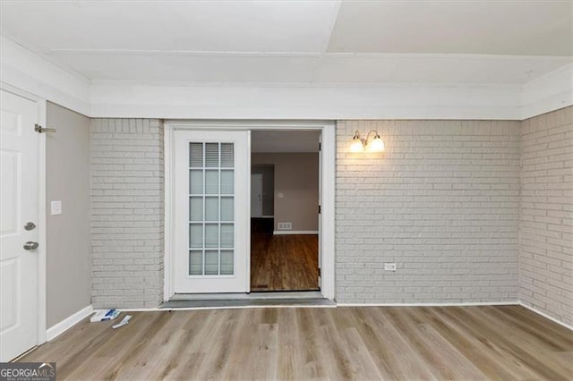 spare room featuring wood-type flooring and brick wall