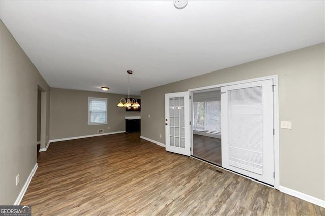 unfurnished living room featuring french doors, hardwood / wood-style flooring, and an inviting chandelier