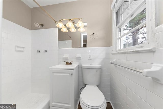 bathroom featuring a tile shower, vanity, tile walls, and toilet