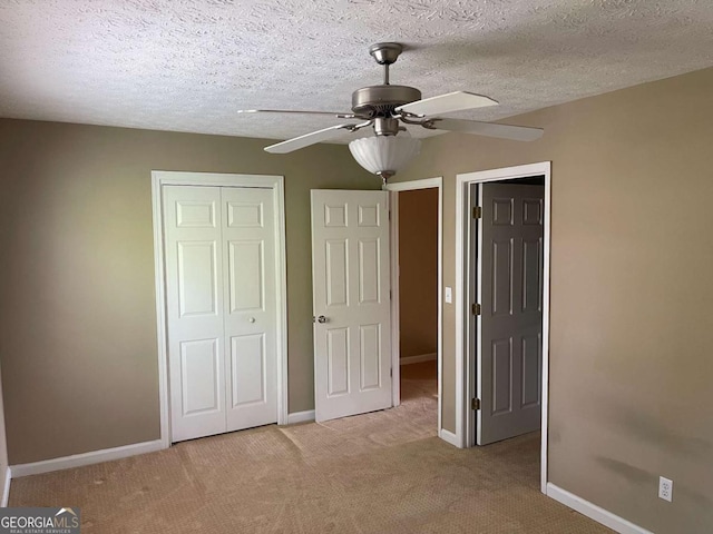 unfurnished bedroom featuring ceiling fan, a closet, light colored carpet, and a textured ceiling