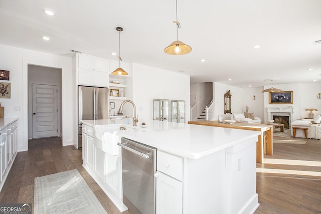 kitchen featuring decorative light fixtures, white cabinets, appliances with stainless steel finishes, and a center island with sink