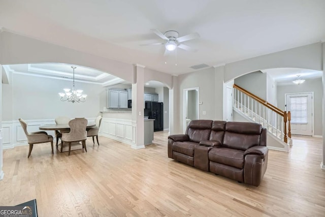 living room featuring a tray ceiling, crown molding, light hardwood / wood-style flooring, and ceiling fan with notable chandelier